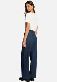 Jeans larges bleu foncé avec taille haute, associés à une chemise blanche à manches courtes. Tissu lisse et détails minimaux.