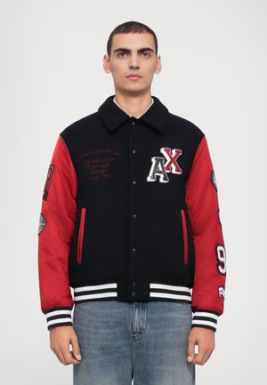 Sort og rød varsity-jakke med knaplukning, stribede manchetter, broderede logoer og patcher på ærmerne. Lavet af stof med en glat overflade.
