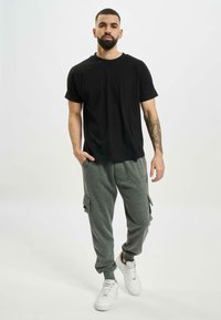 Schwarzes Baumwoll-T-Shirt kombiniert mit grauen Cargo-Sweatpants mit Seitentaschen, abgerundet mit weißen Sneakers. Schlichtes, lässiges Outfit.