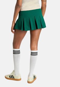Zelená plisovaná sukňa po kolená s hladkým povrchom. V kombinácii s bielymi ponožkami s čiernymi pruhmi a svetlými teniskami.