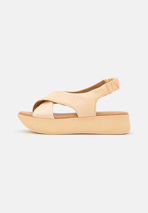 Beige leather wedge sandals with cross-over straps and elastic back. Features a neutral-toned, chunky platform sole for support.