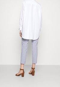 Biała koszula z długim rękawem o luźnym kroju, zestawiona z niebiesko-białymi spodniami culottes w paski oraz brązowymi sandałami na klocku.