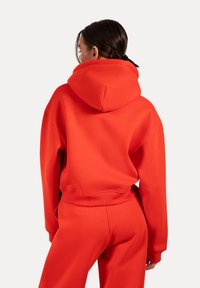 Sweatshirt rouge surdimensionné en tissu doux avec une capuche à cordon et des poignets côtelés, associé à un pantalon rouge assorti.