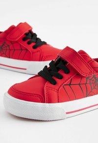 Baskets synthétiques rouges avec un motif de toile d'araignée noir, dotées d'une sangle Velcro et de lacets noirs. Semelle extérieure en caoutchouc blanche avec un motif texturé.