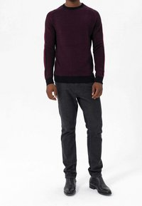 Pull bordeaux foncé à col rond et poignets noirs, avec des rayures contrastantes le long des manches, associé à un pantalon gris foncé et des bottes noires.