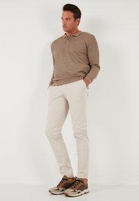 Polo a maniche lunghe beige a coste, pantaloni slim-fit crema e scarpe da ginnastica multicolori con lacci e pannelli a contrasto.
