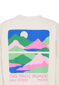 Sweatshirt crème avec un graphisme de montagnes aux nuances de rose, vert et bleu, accompagné du texte : "CE MOMENT MAGIQUE PROTESTATION DU LEVER DE SOLEIL TÔT."