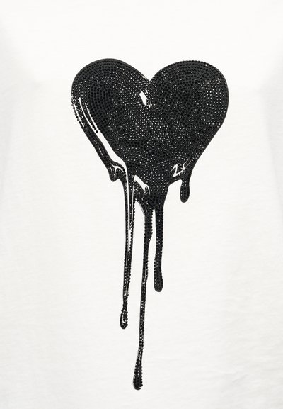 Λευκό μπλουζάκι με μαύρη καρδιά από στρας που στάζει προς τα κάτω. Η καρδιά είναι γυαλιστερή και υφή, τονίζοντας το εφέ του στάξιμου.