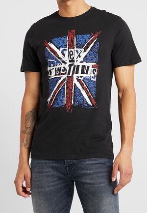 Man wearing black T-shirt with distressed Union Jack and "Sex Pistols" text graphic, paired with blue jeans.