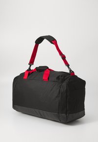 Bolsa de deporte negra con correas rojas, con un exterior de tela durable, asa superior y una base negra lisa y brillante.