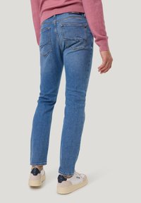 Blaue Denim-Jeans mit slim fit, ausgestattet mit zwei Gesäßtaschen und Stickdetails, kombiniert mit weißen Sneakers und einem rosa Pullover.