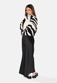 Sorte og hvide zebra-stribede oversized trøje, sort satin maxi nederdel og sorte platform sandaler, der viser en afslappet, lagdelt stil.