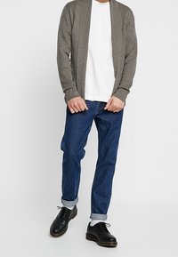 Gray knitted cardigan, white crew-neck t-shirt, blue jeans with rolled cuffs, and black lace-up shoes. Simple design, casual fit.