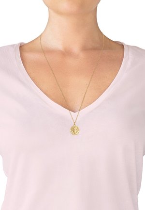 Collana con pendente d'oro su una catena sottile, caratterizzata da un ciondolo rotondo con incisioni dettagliate, indossata sopra un top a V di colore rosa chiaro.