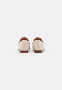 Mocassins en cuir beige avec un bout arrondi, un design minimaliste et un talon plat en bois. Texture lisse, sans motifs ni accessoires visibles.