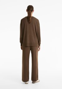 Maglione in maglia marrone oversize con maniche lunghe e polsini a costine, abbinato a pantaloni a gamba larga coordinati, visto da dietro.