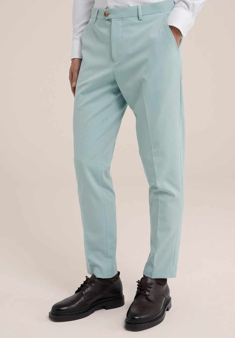 Light mint green trousers with a smooth texture, tapered fit, side pockets, and a front button closure, paired with black lace-up shoes.