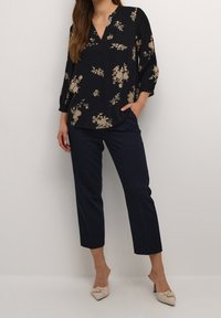 Blusa floral azul marino con mangas de tres cuartos y escote en V, combinada con pantalones azul marino ajustados y zapatos de tacón alto beige con nudo.