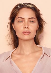 Ljusrosa blus med krage, mjuk textur och ömtålig glans. Modellen har naturlig sminkning och vågigt, axellångt hår.