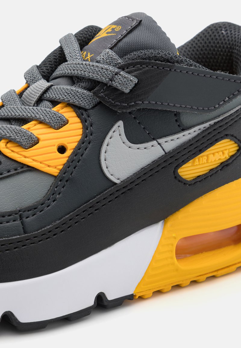 Zapatillas Nike Air Max de cuero gris oscuro, con acentos en amarillo y gris, lengüeta texturizada y amortiguación visible en la suela blanca.