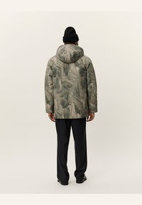 Chaqueta abstracta gris con un patrón, con capucha, hecha de una tela texturizada, combinada con pantalones negros y un gorro a juego.