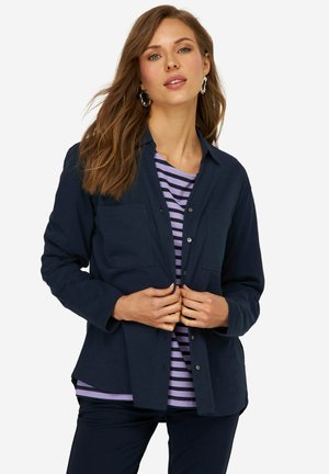 Marineblause button-up Hemd mit zwei Brusttaschen, über einem lila-weißen gestreiften Oberteil getragen, mit langen Ärmeln und einem lässigen Schnitt.