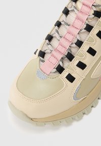 Zapatillas de deporte beige y rosa con puntera, cordones negros y blancos, tejido de malla, superposiciones de cuero y suela de goma resistente sobre un fondo blanco.