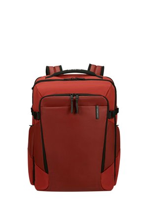 Zaino rettangolare rosso con spallacci imbottiti, tasca frontale con cerniera, tasche laterali e dettagli con cerniere nere, in piedi su sfondo bianco.