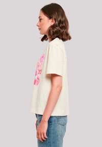 Cream short-sleeve t-shirt featuring colorful heart and smiley face graphics on the front. Worn with light blue jeans.