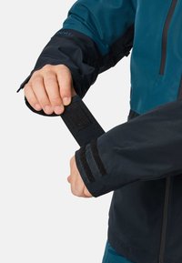 Person adjusting black velcro wrist strap on a blue and black waterproof jacket sleeve.