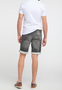 Shorts en jean gris avec ourlets roulés, deux poches arrière et un léger dégradé. Associés à un t-shirt blanc ajusté et des chaussures marron.