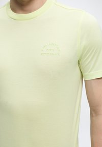 Άνδρας που φοράει ανοιχτόκίτρινη κοντομάνικη μπλούζα με κεντημένο το κείμενο «Karl Lagerfeld Paris 21 Rue St-Guillaume» στο στήθος.