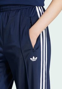 Marina idrottsbyxor med vita sidostriped och en broderad logotyp. Har en diskret ficka med dragkedja och ett elastiskt midjeband för komfort.