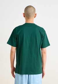 T-shirt en coton vert avec un col rond classique, des manches courtes et une coupe décontractée, affiché de l'arrière. Texture lisse, sans motifs visibles.