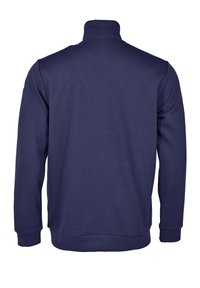 Tummansininen vetoketjullinen neule, jossa on korkea kaulus, pitkät hihat, ribbaatut hihansuut ja vyötärö. Valmistettu sileästä puuvillakankaasta, ei näkyvissä olevia logoja.