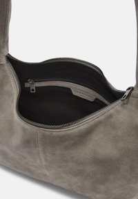 Szara torebka z zamszu z otwartym górnym zamkiem, ukazująca czarne materiałowe wnętrze oraz wewnętrzną kieszeń zapinaną na zamek z metką marki.