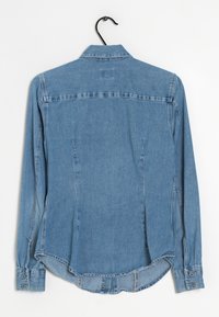 Camicia di denim azzurro chiaro con maniche lunghe, polsini a bottoni, colletto a punta e orlo curvo. Presenta cuciture laterali e una texture sottile.