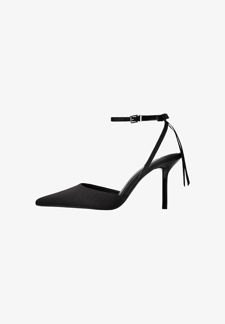 Pump nera con tacco alto, punta affusolata, finitura in satin, cinturino alla caviglia con fibbia e tacco sottile. La vista laterale mette in mostra il design elegante.