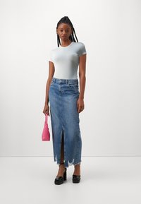 Top fitted azzurro chiaro a maniche corte abbinato a una lunga gonna di jeans blu con uno spacco frontale e orlo sfilacciato. Accessoriato con una borsa rosa.