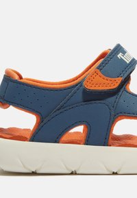 Blaue und orangefarbene Kindersandale mit einem strukturierten Synthetikobermaterial, Schaumstofffutter, verstellbarem Riemen und einer weißen Gummisohle mit Zickzackmuster.