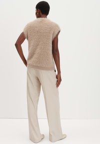 Maglione smanicato beige in peluche con finitura testurizzata, abbinato a pantaloni a gamba larga beige chiaro. Dettaglio di orlo sottile in vita.