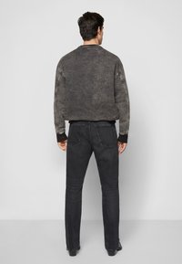 Gray faded sweatshirt with dark ribbed cuffs, paired with black jeans. The outfit features a relaxed fit and visible stitching details.