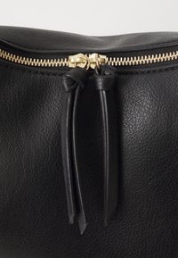 Clutch in pelle nera con finitura testurizzata, dotata di chiusura con zip dorata e due nappine in pelle attaccate al cursore della zip.