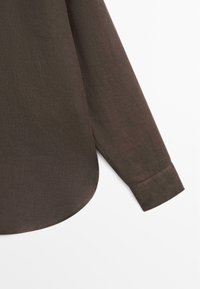 Bruine bloes met lange mouwen, een afgeronde zoom en een manchet met knopen, getoond tegen een witte achtergrond.