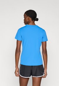 Modra športna majica s kratkimi rokavi iz lahkega blaga, ki ima oprijet kroj in okrogel izrez, v kombinaciji s črnimi kratkimi hlačami.