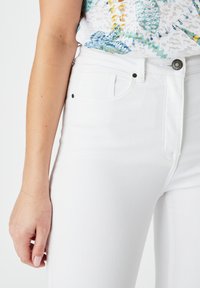 Jeans de denim blanco con un corte slim, que cuentan con bolsillos frontales, un botón de metal y detalles de costura sutiles. La textura parece suave.