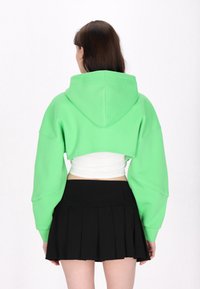 Felpa verde tagliata con cappuccio e maniche lunghe, abbinata a una gonna plissettata nera. Tessuto liscio, colore vivace e design casual.