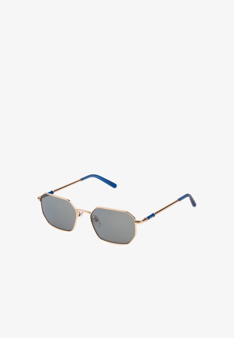 Lunettes de soleil hexagonales à verres gris avec fines montures métalliques dorées et extrémités de branches bleues, montrées légèrement de biais sur fond blanc.