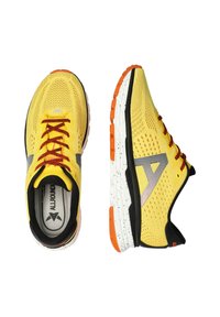 Gelbe Sportschuhe mit Netz-Obermaterial, roten Schnürsenkeln, schwarzen und grauen Akzenten sowie einer weiß gesprengelten Sohle. Verfügt über eine orange Ferse und Markenkennzeichnung.