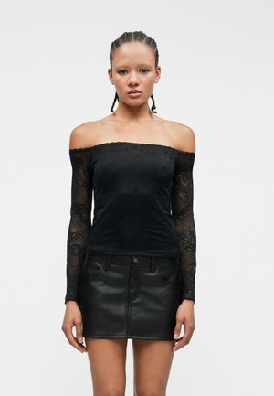 Czarny top typu off-the-shoulder z długimi koronkowymi rękawami, zdobiony kwiatowymi wzorami; zestawiony z czarną skórzaną mini spódnicą.